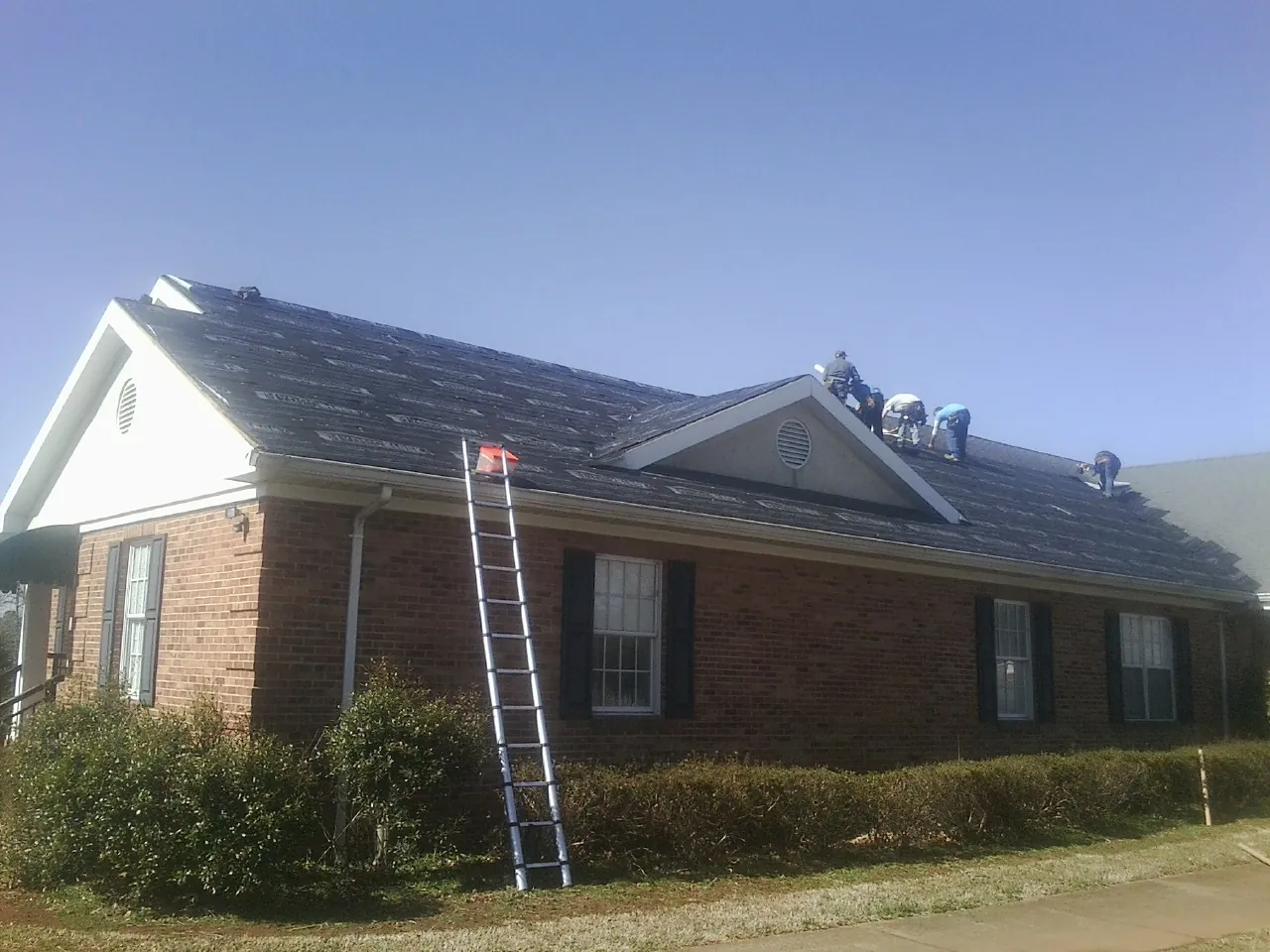 Crew tearing shingles off a brick ranch roof with a ladder set — Emergency Roof Repair work by our crew in Georgetown
